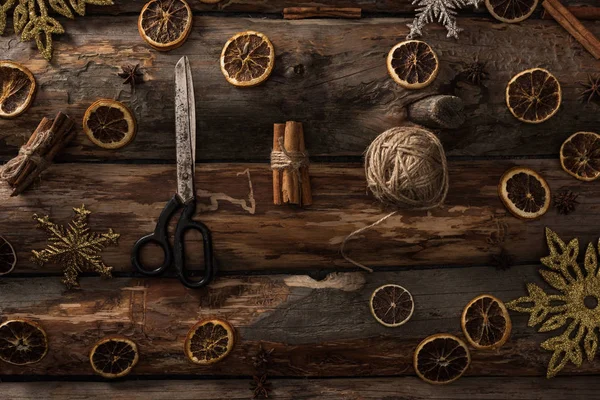 Flat lay with cinnamon sticks, scissors, ball of thread on wooden background with winter decor — Stock Photo