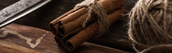 Close up view of cinnamon sticks, scissors, ball of thread on wooden background, panoramic shot — Stock Photo