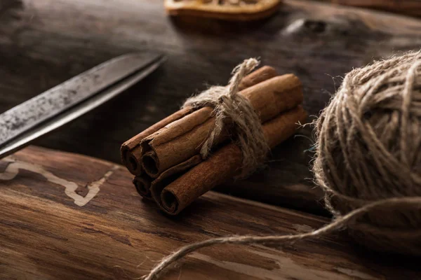 Close up view of cinnamon sticks, scissors, ball of thread on wooden background — Stock Photo