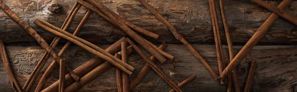 Top view of cinnamon sticks scattered on wooden background, panoramic shot — Stock Photo