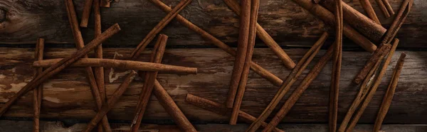 Vista superior de paus de canela espalhados no fundo de madeira, tiro panorâmico — Fotografia de Stock