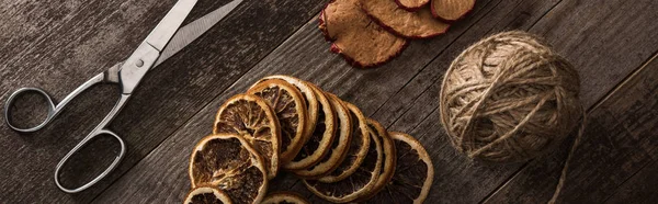 Vue de dessus du fil, des ciseaux et des tranches d'agrumes et de pommes séchées sur fond en bois, vue panoramique — Photo de stock