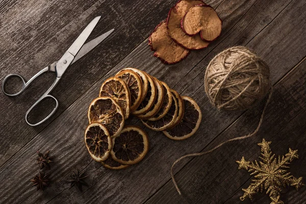 Vista dall'alto di filo, forbici e fette di agrumi e mele essiccate su fondo di legno con fiocco di neve — Foto stock
