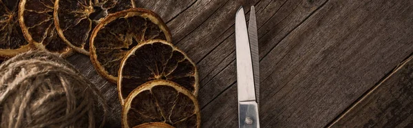 Top view of thread, scissors and dried citrus slices on wooden background, panoramic shot — Stock Photo