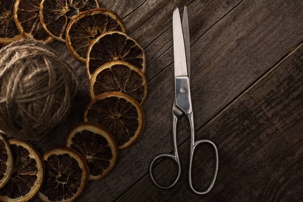 Top view of thread, scissors and dried citrus slices on wooden background — Stock Photo