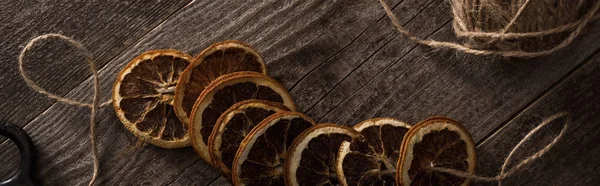 Top view of thread with dried citrus slices on wooden background, panoramic shot — Stock Photo