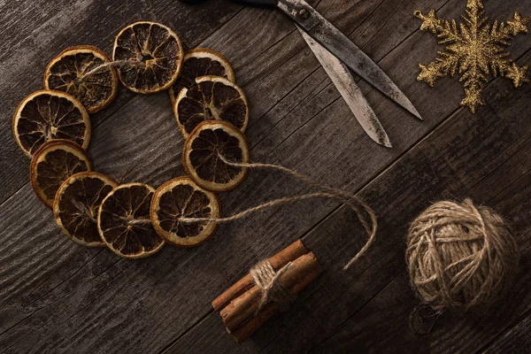 Top view of dried citrus slices on rope near snowflake, cinnamon and scissors on wooden surface — Stock Photo