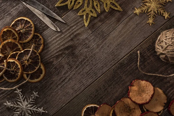 Vista superior de cítricos secos y rodajas de manzana cerca de copos de nieve, cuerda y tijeras en superficie de madera con espacio para copiar - foto de stock