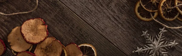 Top view of dried citrus and apple slices near snowflake on wooden surface with copy space, panoramic shot — Stock Photo