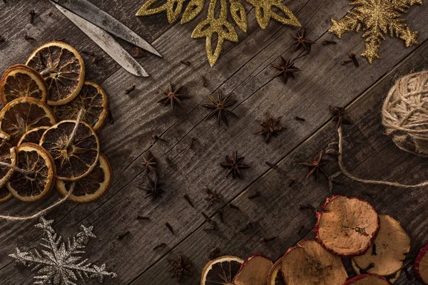 Draufsicht auf getrocknete Zitrus- und Apfelscheiben in der Nähe von Schneeflocken, Schere, Faden und Anis auf Holzoberfläche — Stockfoto