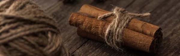 Selective focus of ball of thread and cinnamon sticks on wooden surface, panoramic shot — Stock Photo