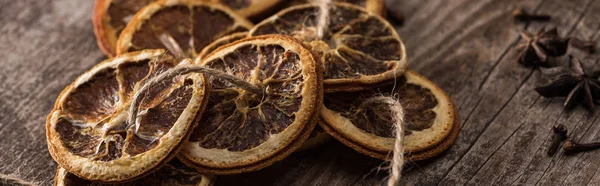 Rodajas de cítricos secos en la cuerda cerca de anís en la superficie de madera, plano panorámico - foto de stock