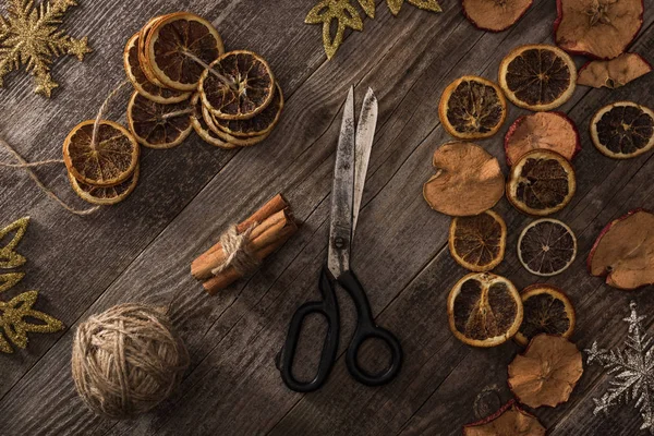 Top view of dried citrus and apple slices near snowflakes, scissors, thread and cinnamon on wooden surface — Stock Photo