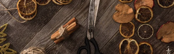 Top view of dried citrus and apple slices near snowflakes, scissors, thread and cinnamon on wooden surface, panoramic shot — Stock Photo