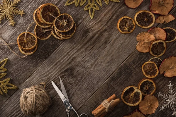 Draufsicht auf getrocknete Zitrus- und Apfelscheiben in der Nähe von Schneeflocken, Schere, Faden und Zimt auf Holzoberfläche mit Kopierraum — Stockfoto
