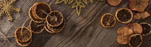Top view of dried citrus and apple slices near snowflakes on wooden surface, panoramic shot — Stock Photo