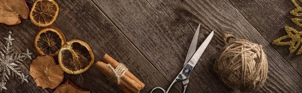 Top view of dried citrus and apple slices near snowflakes, scissors, thread on wooden surface, panoramic shot — Stock Photo