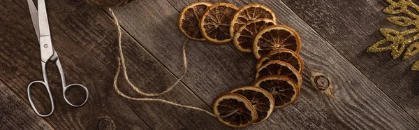 Top view of dried citrus slices on rope near snowflake, scissors on wooden surface, panoramic shot — Stock Photo