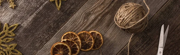 Top view of dried citrus slices near snowflakes, thread, scissors on wooden surface, panoramic shot — Stock Photo