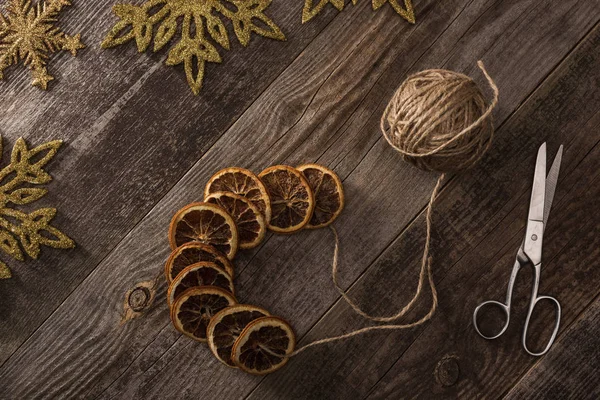 Top view of dried citrus slices on rope near snowflakes, scissors on wooden surface — Stock Photo