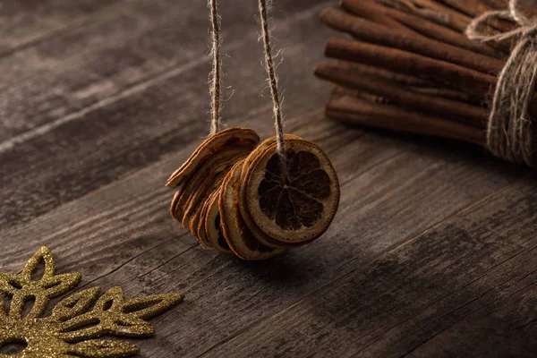 Dried citrus slices on thread near cinnamon and snowflake on wooden background — Stock Photo