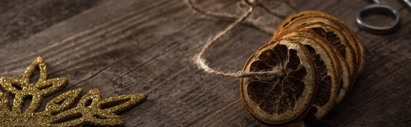 Dried citrus slices on thread near snowflake on wooden background, panoramic shot — Stock Photo