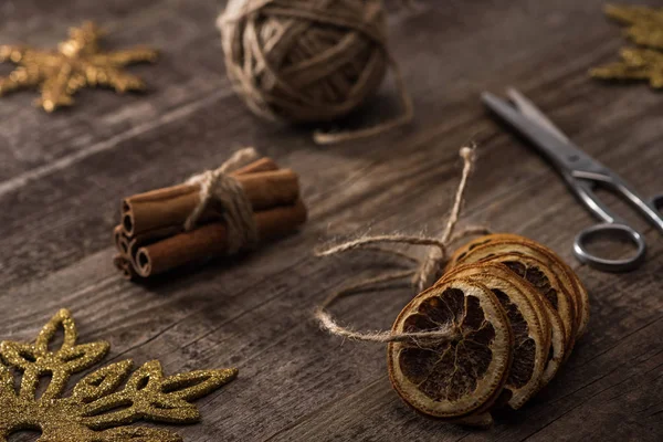 Selective focus of dried citrus slices on thread near cinnamon, scissors and snowflakes on wooden background — Stock Photo