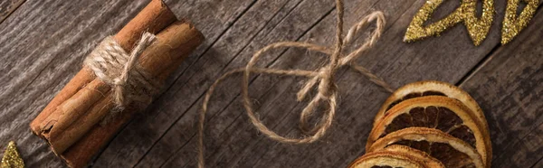 Top view of dried citrus slices on thread near cinnamon and snowflakes on wooden background, panoramic shot — Stock Photo