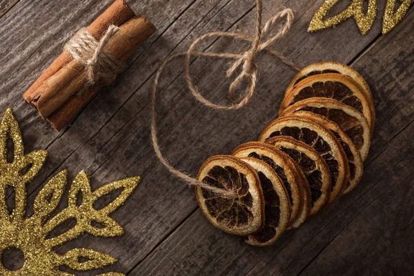 Top view of dried citrus slices on thread near cinnamon and snowflakes on wooden background — Stock Photo