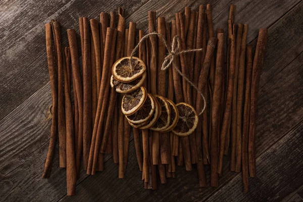 Top view of dried orange slices on thread and cinnamon on wooden background — Stock Photo