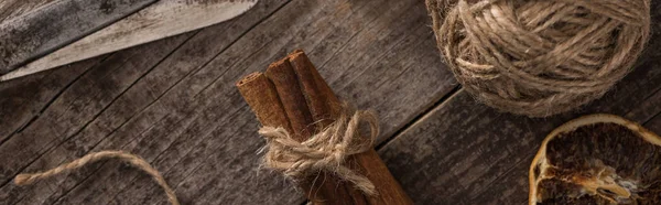 Vista dall'alto di fetta di agrumi secca vicino a palla di filo, cannella e forbici su superficie di legno, colpo panoramico — Foto stock