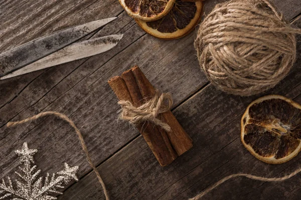 Top view of dried citrus slices near snowflake, ball of thread, cinnamon and scissors on wooden surface — Stock Photo