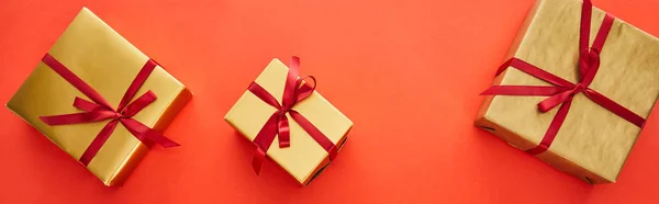 Vue du dessus des boîtes-cadeaux dorées sur fond rouge, panoramique — Photo de stock