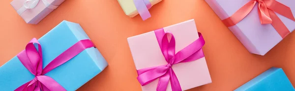 Top view of multicolored gift boxes with ribbons and bows on orange background, panoramic shot — Stock Photo