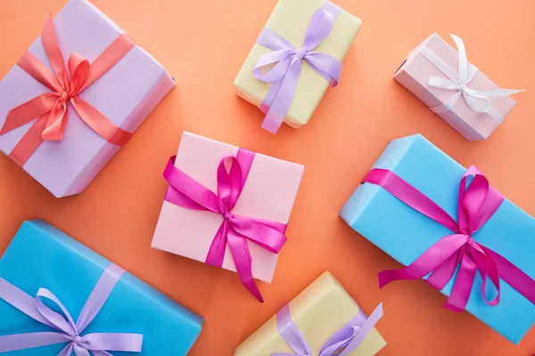 Top view of multicolored gift boxes with ribbons and bows on orange background — Stock Photo