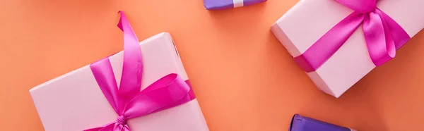 Top view of pink and purple gift boxes with ribbons and bows on orange background, panoramic shot — Stock Photo