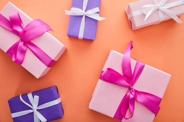 Vista superior de las cajas de regalo de color rosa y púrpura con cintas y arcos sobre fondo naranja - foto de stock