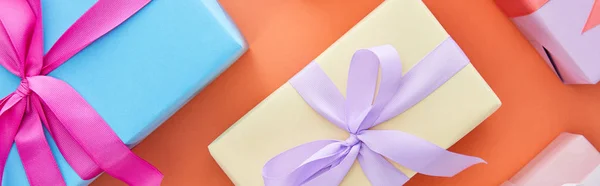 Top view of multicolored gift boxes with ribbons and bows on orange background, panoramic shot — Stock Photo