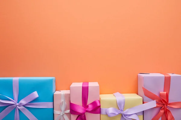Flat lay with multicolored gift boxes with ribbons and bows on orange background with copy space — Stock Photo