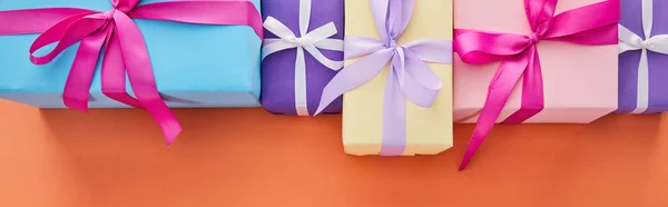 Pose plate avec des boîtes-cadeaux multicolores avec des rubans et des arcs sur fond orange avec espace de copie, vue panoramique — Photo de stock