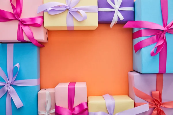 Square frame of multicolored gift boxes with ribbons and bows on orange background with copy space — Stock Photo