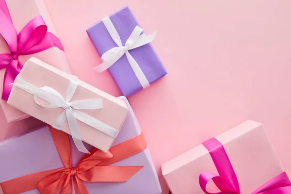 Top view of colorful gift boxes with ribbons and bows scattered on pink background — Stock Photo