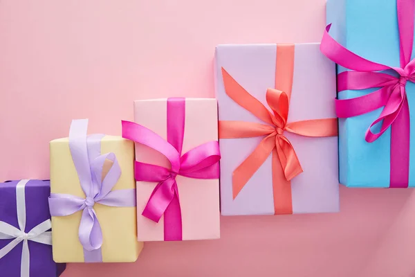 Flat lay with colorful gift boxes with ribbons and bows scattered on pink background with copy space — Stock Photo