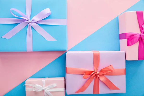 Draufsicht auf bunte Geschenkboxen mit Bändern und Schleifen auf blauem und rosa Hintergrund — Stockfoto