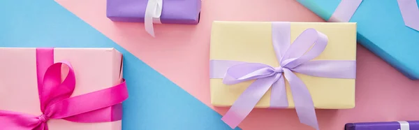 Top view of colorful gift boxes with ribbons and bows on blue and pink background, panoramic shot — Stock Photo