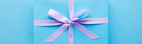 Top view of blue gift with violet ribbon on blue background, panoramic shot — Stock Photo