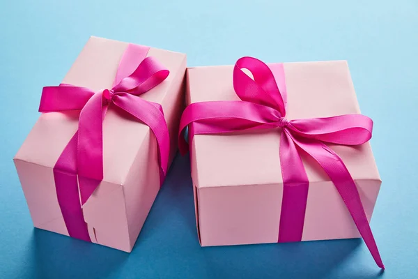 Boîtes-cadeaux roses colorées avec rubans cramoisis et noeuds sur fond bleu — Photo de stock