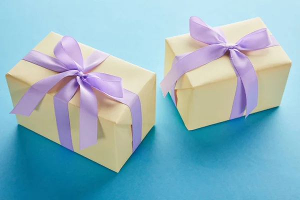 Cajas de regalo de colores amarillos con cintas violetas y arcos sobre fondo azul - foto de stock