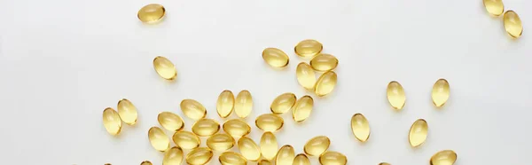 Top view of golden fish oil capsules scattered on white background, panoramic shot — Stock Photo