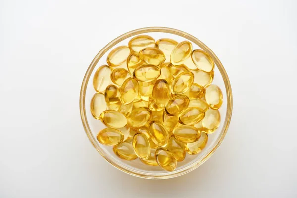 Top view of golden fish oil capsules in glass bowl on white background — Stock Photo